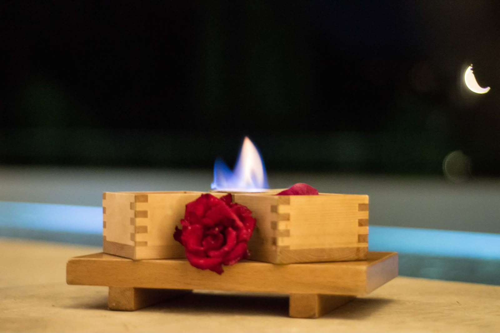 Wooden masu serve lit with a blue flame beside the pool at night