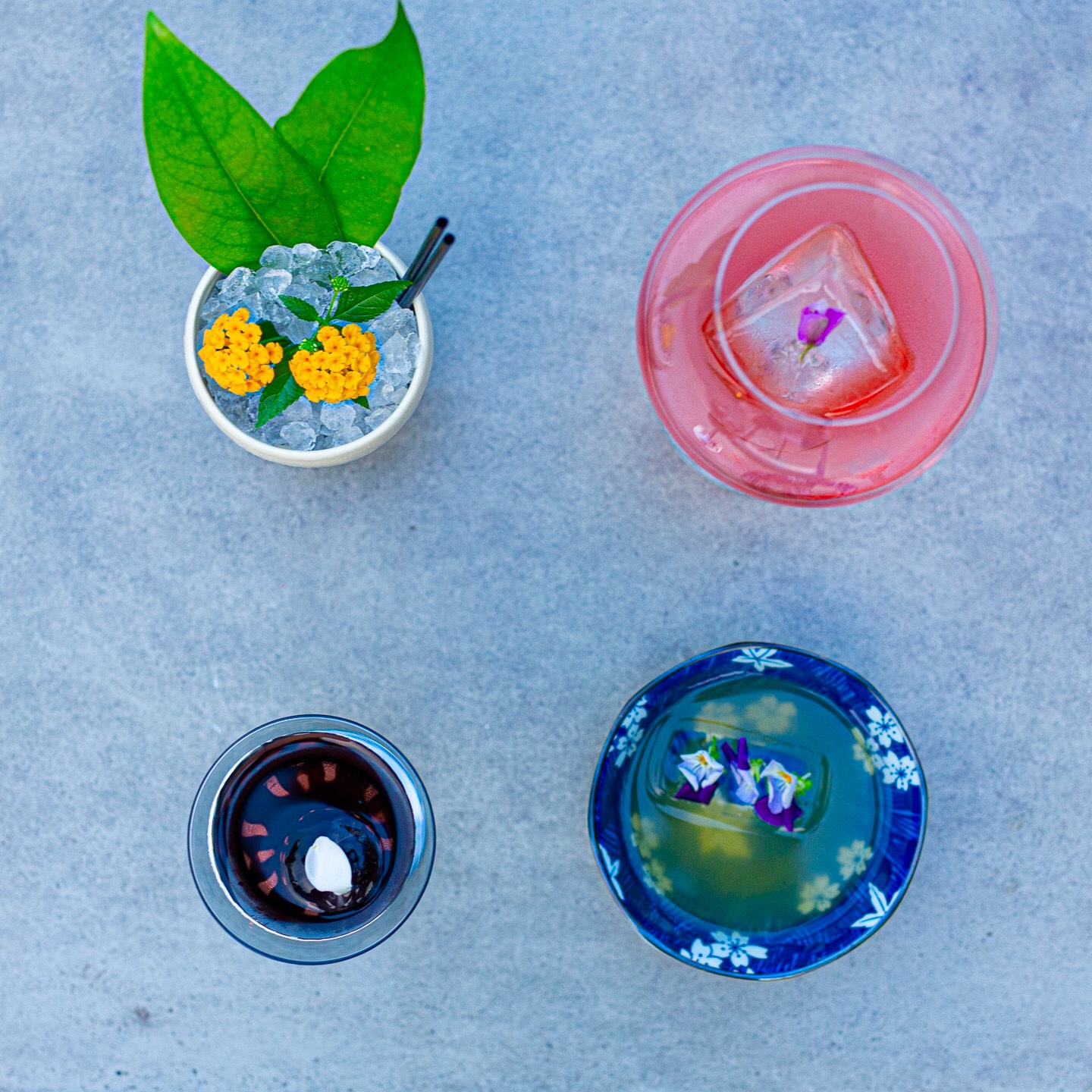 Overhead view of four cocktails on concrete, from crushed ice to clarified serves