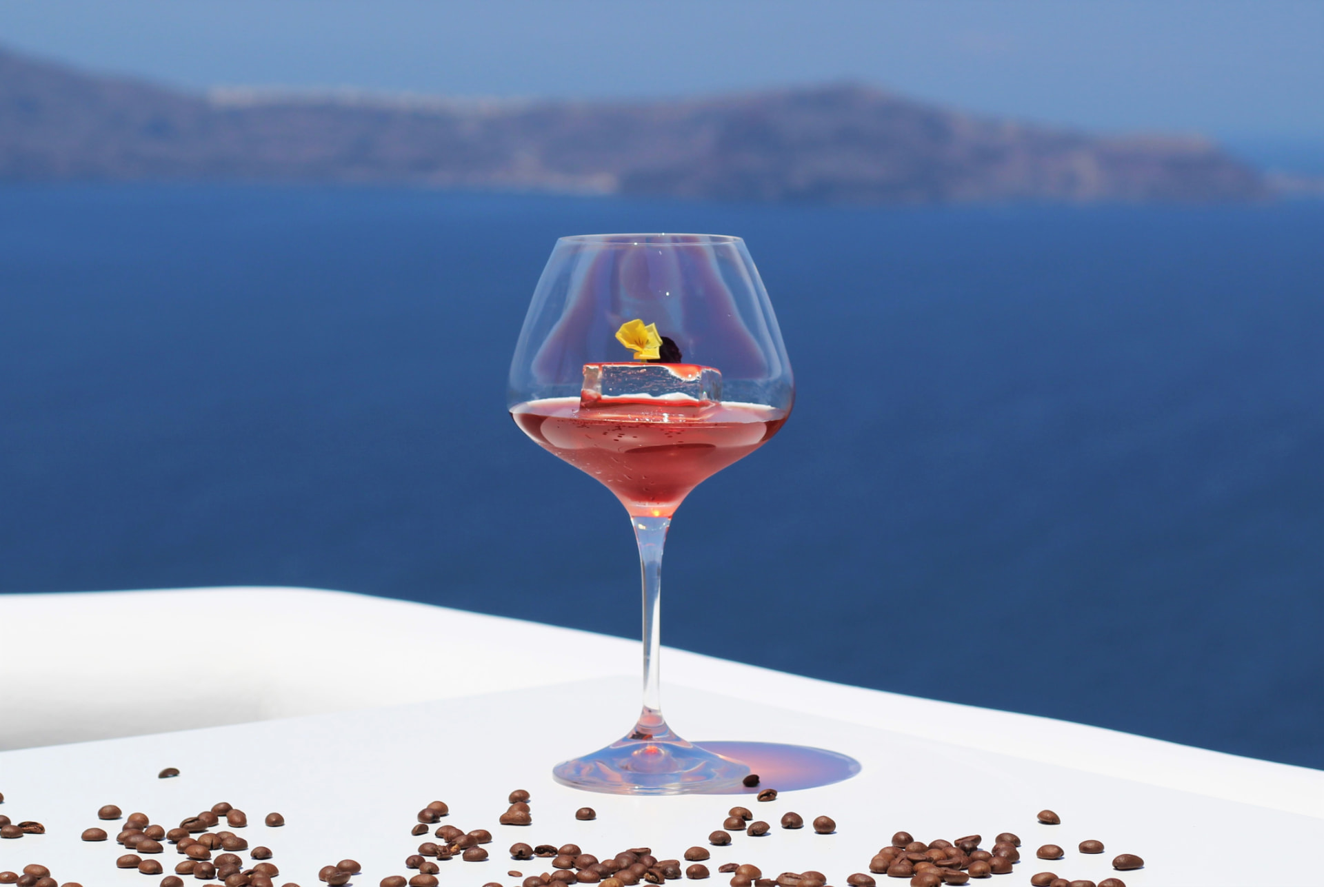 Rosé cocktail in a stemmed glass with clear ice and coffee beans, caldera behind