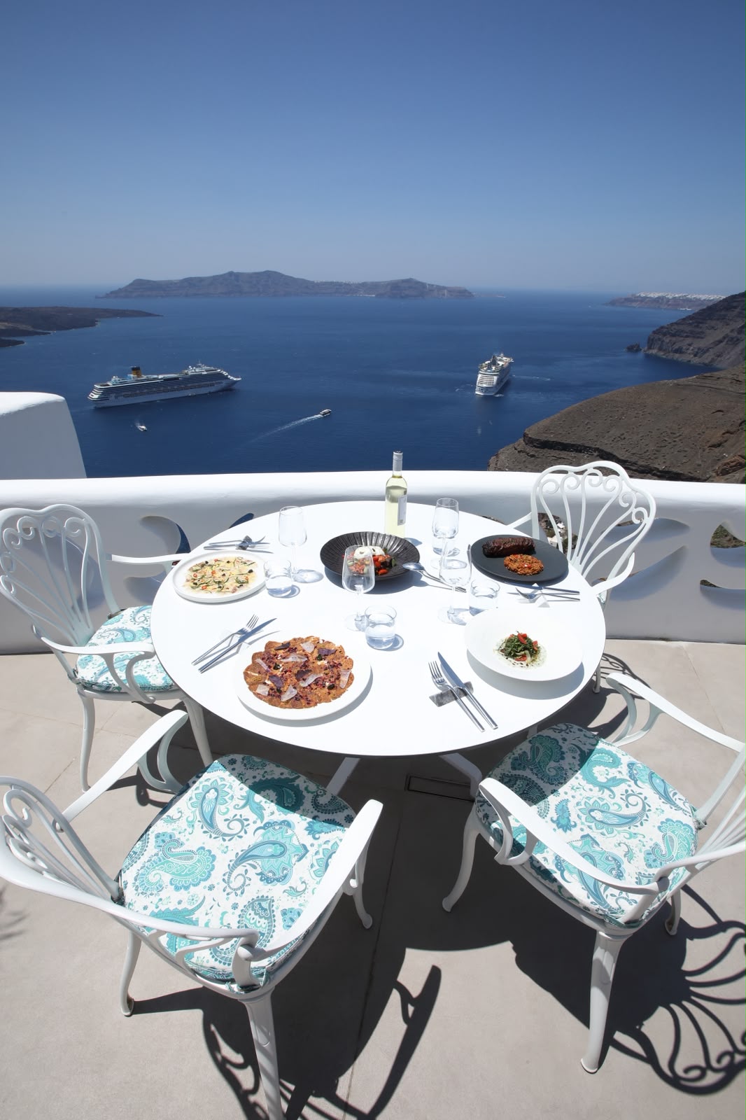 Round terrace table set for four with the caldera and cruise ships behind