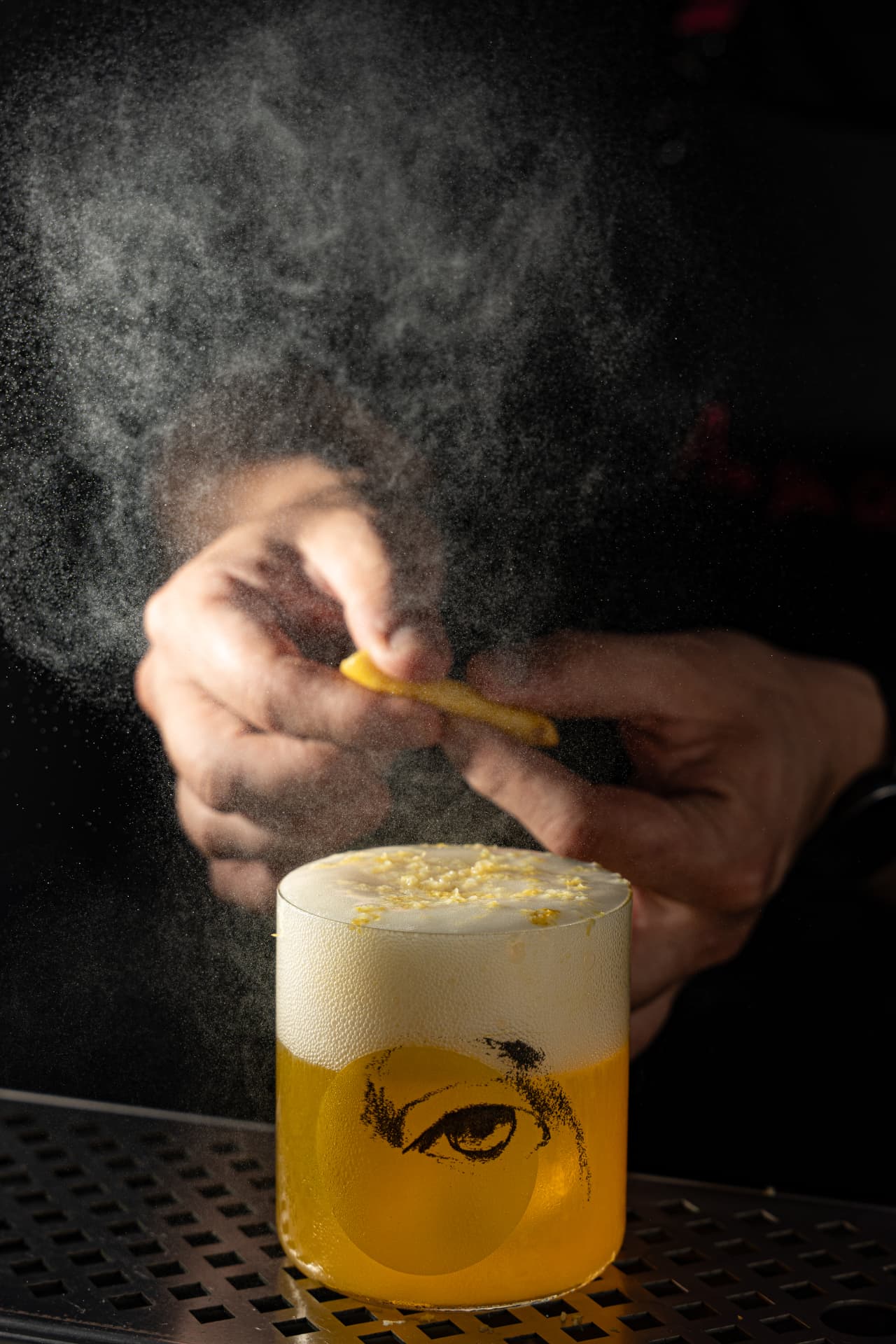 Bartender expressing citrus oils over a foamed sour in low light