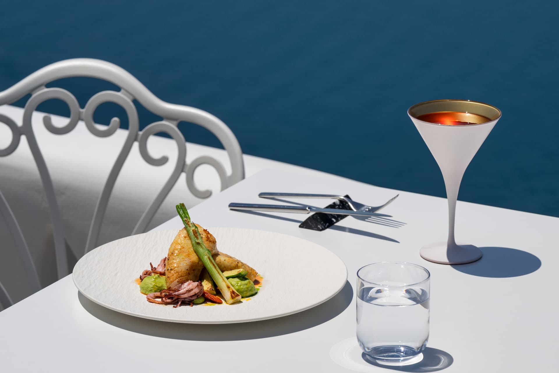 Squid main course with a signature cocktail on a terrace table above the water