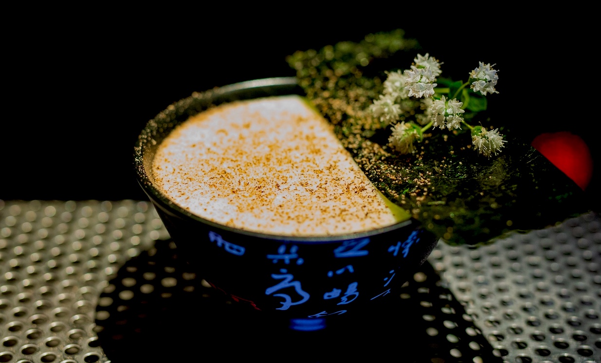 Foamed cocktail dusted with spice in a blue ceramic bowl with wild flowers