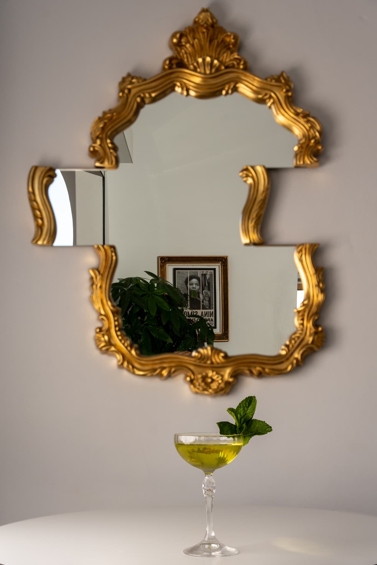 Green herbal cocktail on a white table beneath a gilded baroque mirror