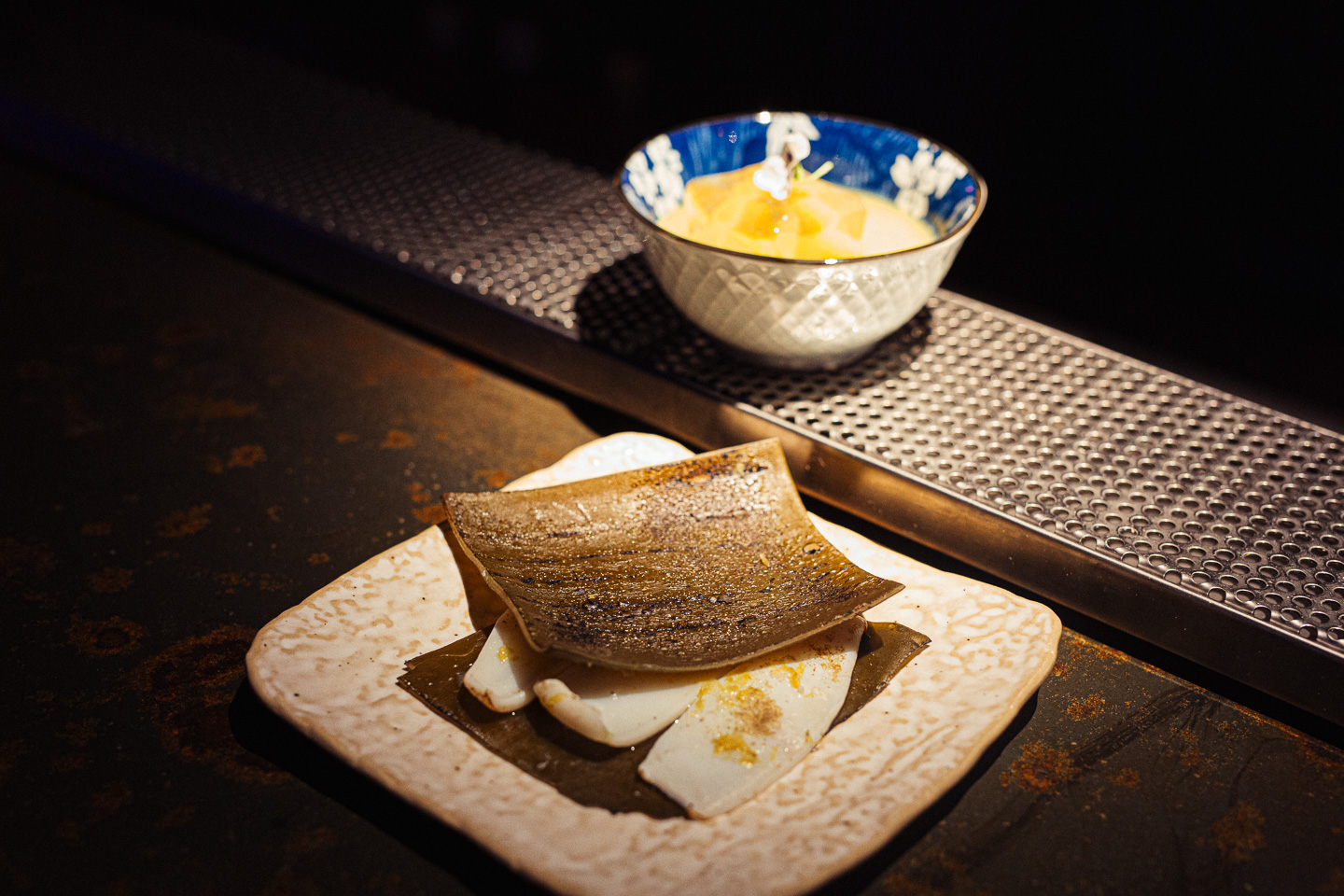 Bar snack of grilled squid on a ceramic plate beside a small citrus serve