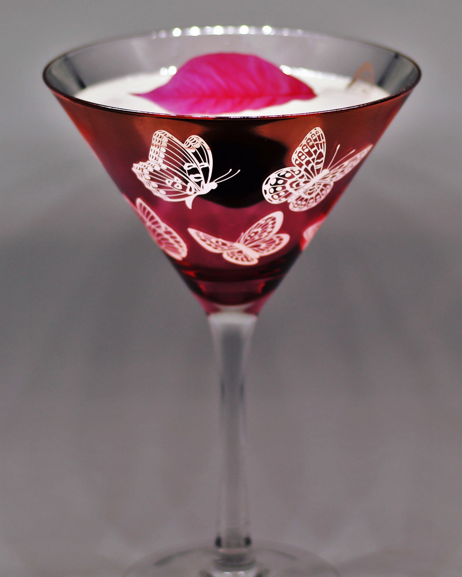 Butterfly-etched martini glass with a foamed serve and pink petal