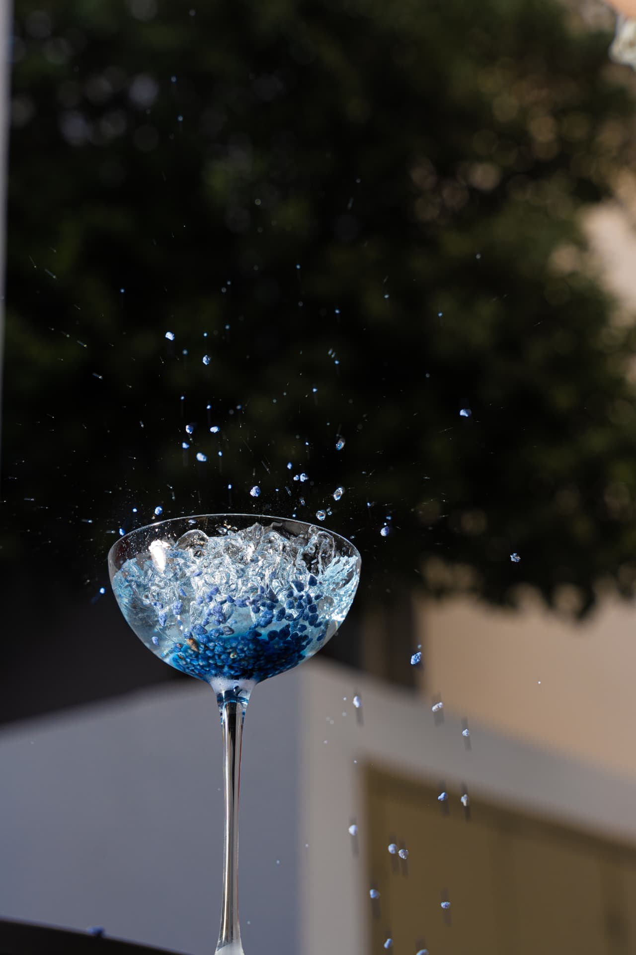 Blue cocktail with sugar spheres splashing against the Santorini greenery