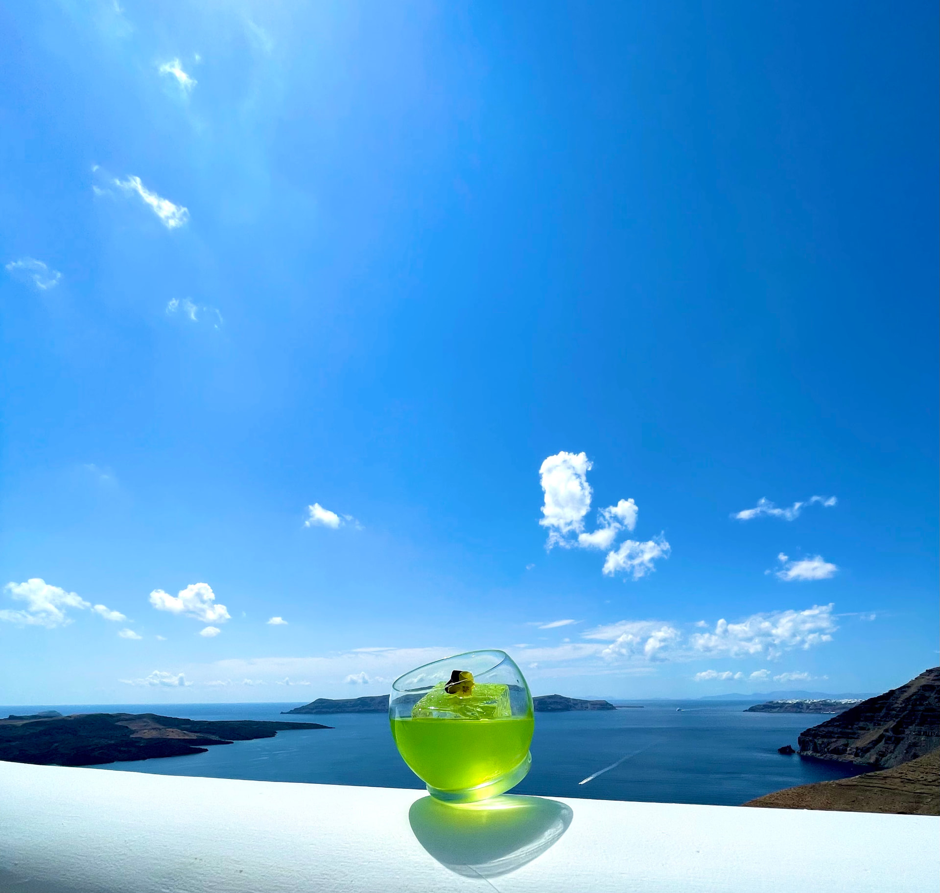 Signature green cocktail on a white ledge above the Santorini caldera