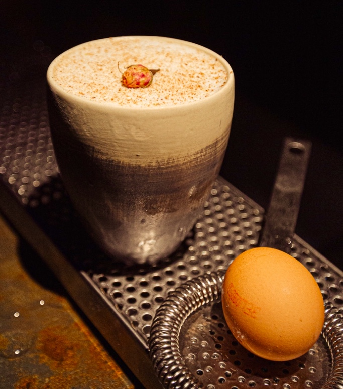 Foamed cocktail in a glazed ceramic cup with a rosebud, egg alongside