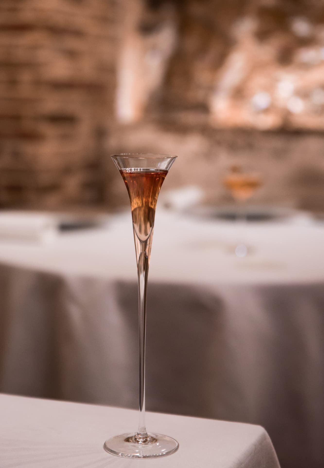 Slim flute of rosé cocktail against the exposed brick dining room