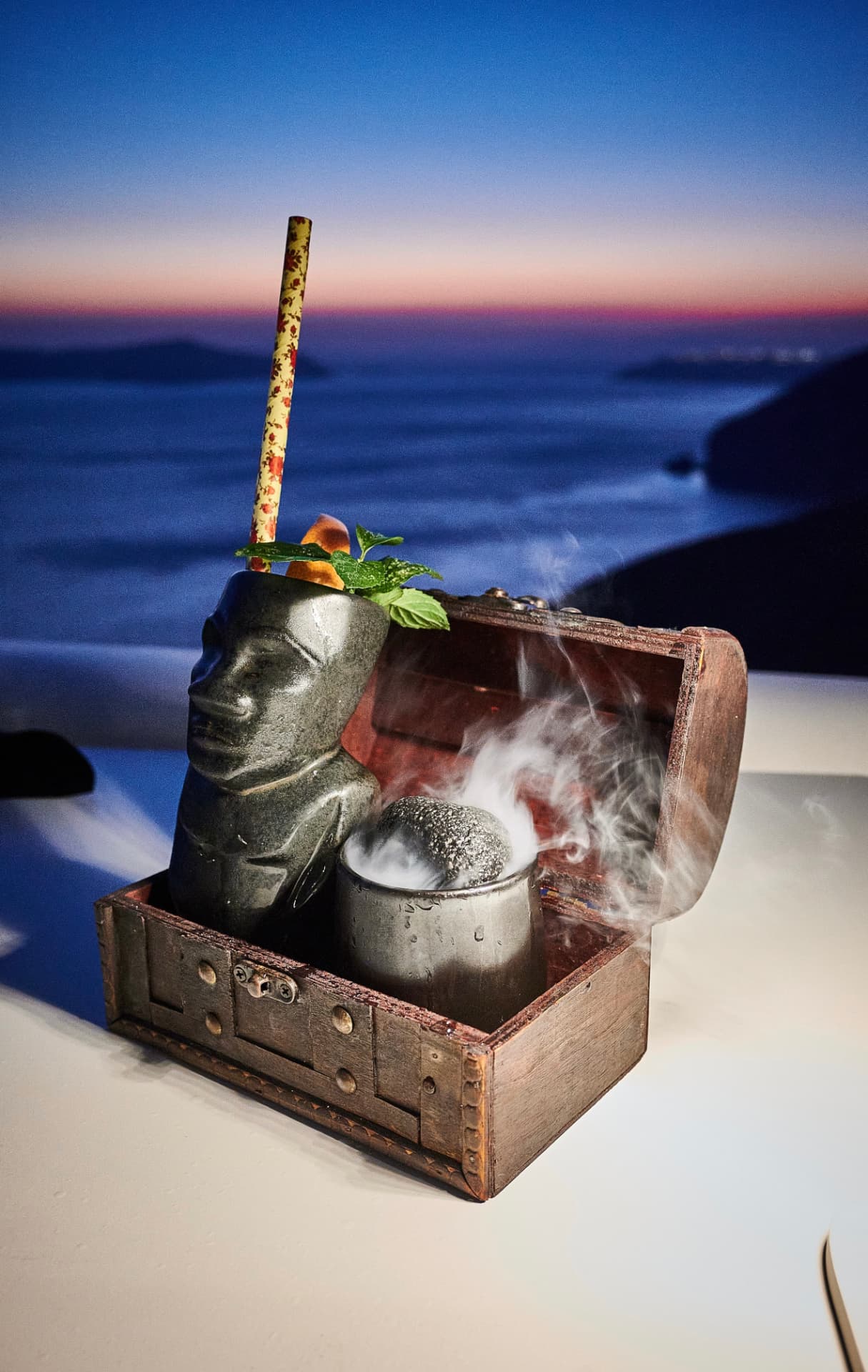 Tiki-style serve in a wooden chest with smoke at blue hour