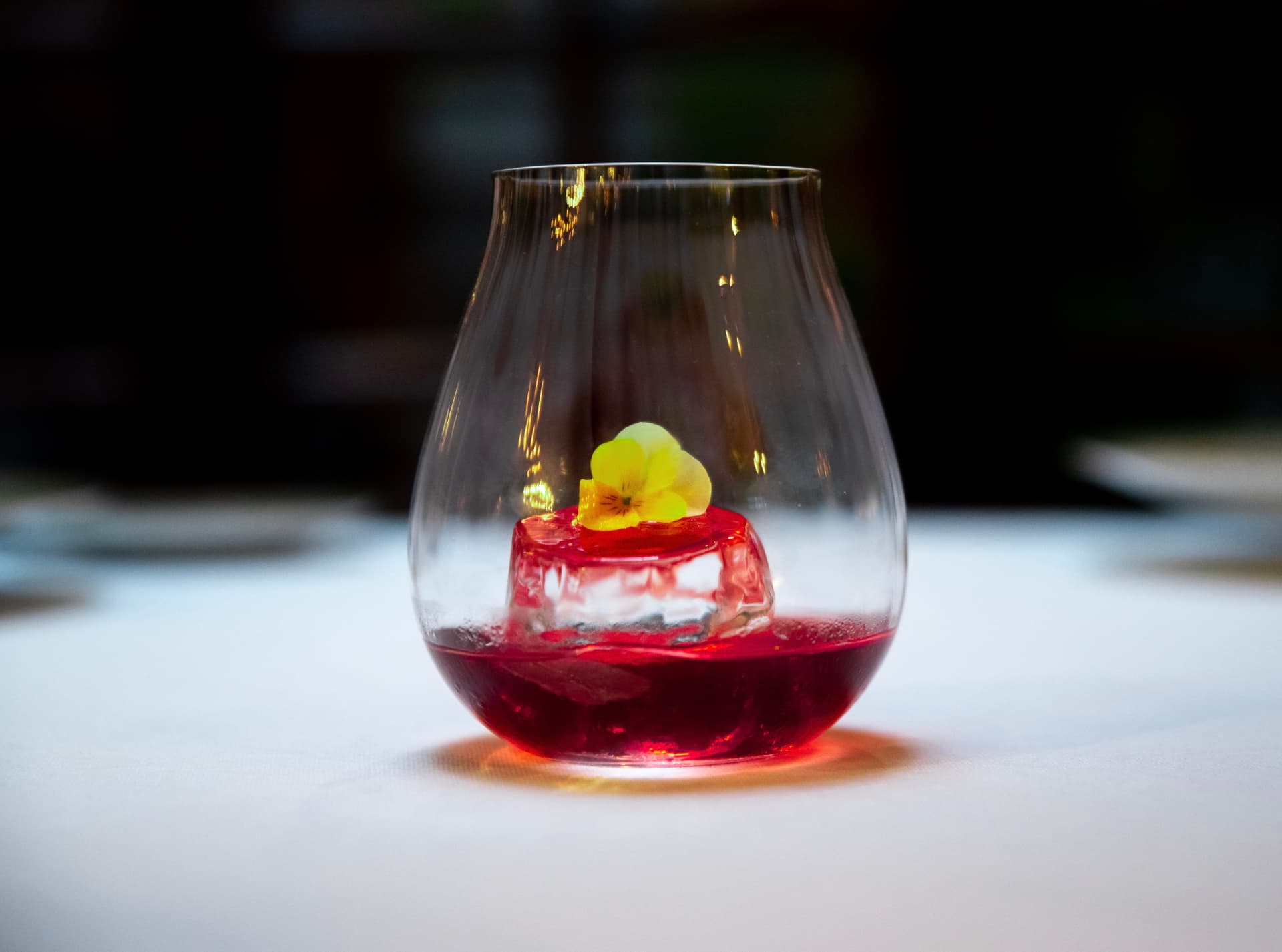 Red aperitif in a fluted tumbler with a clear ice block and yellow blossom