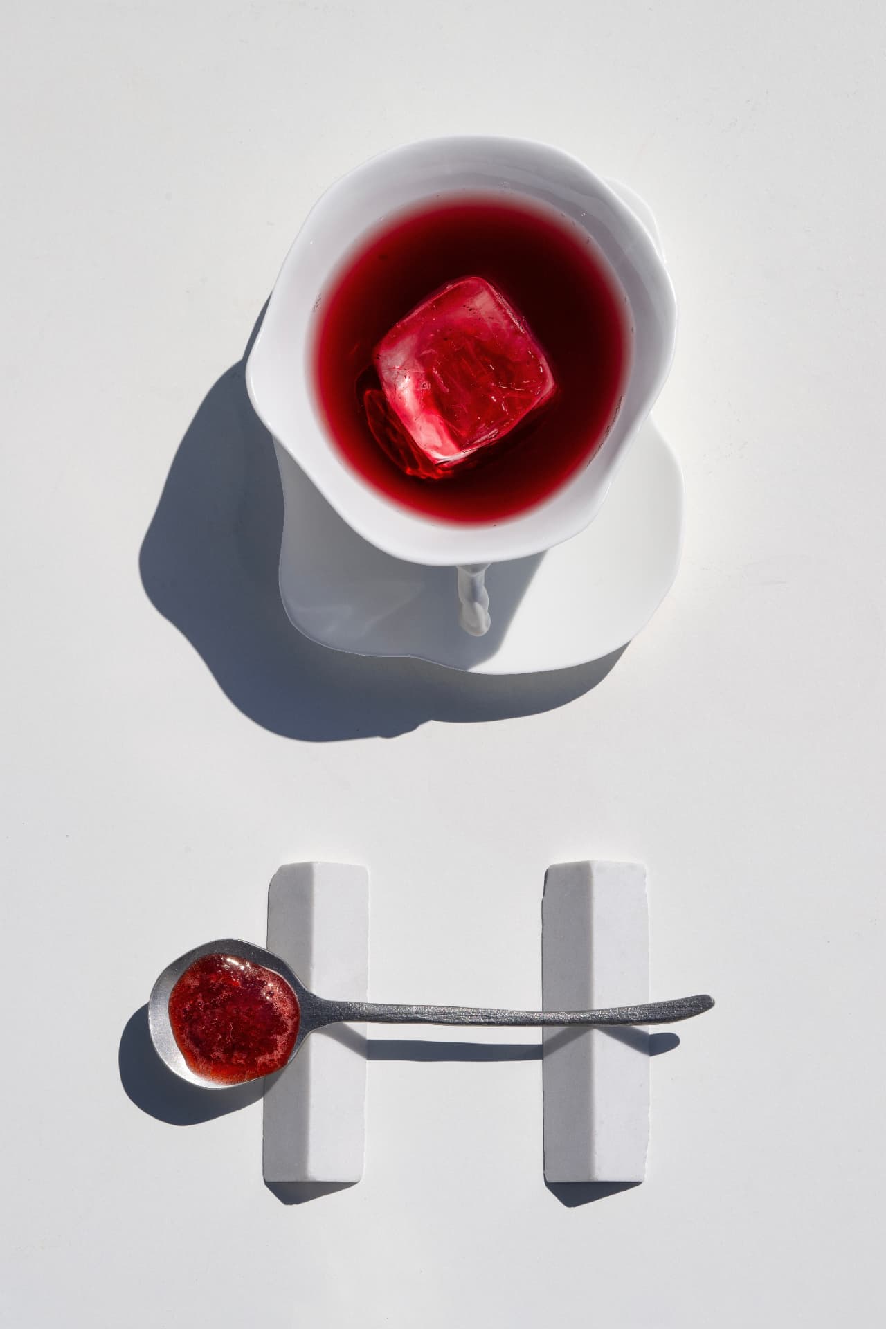 Deep red serve in a porcelain cup with a stained ice cube and preserve spoon