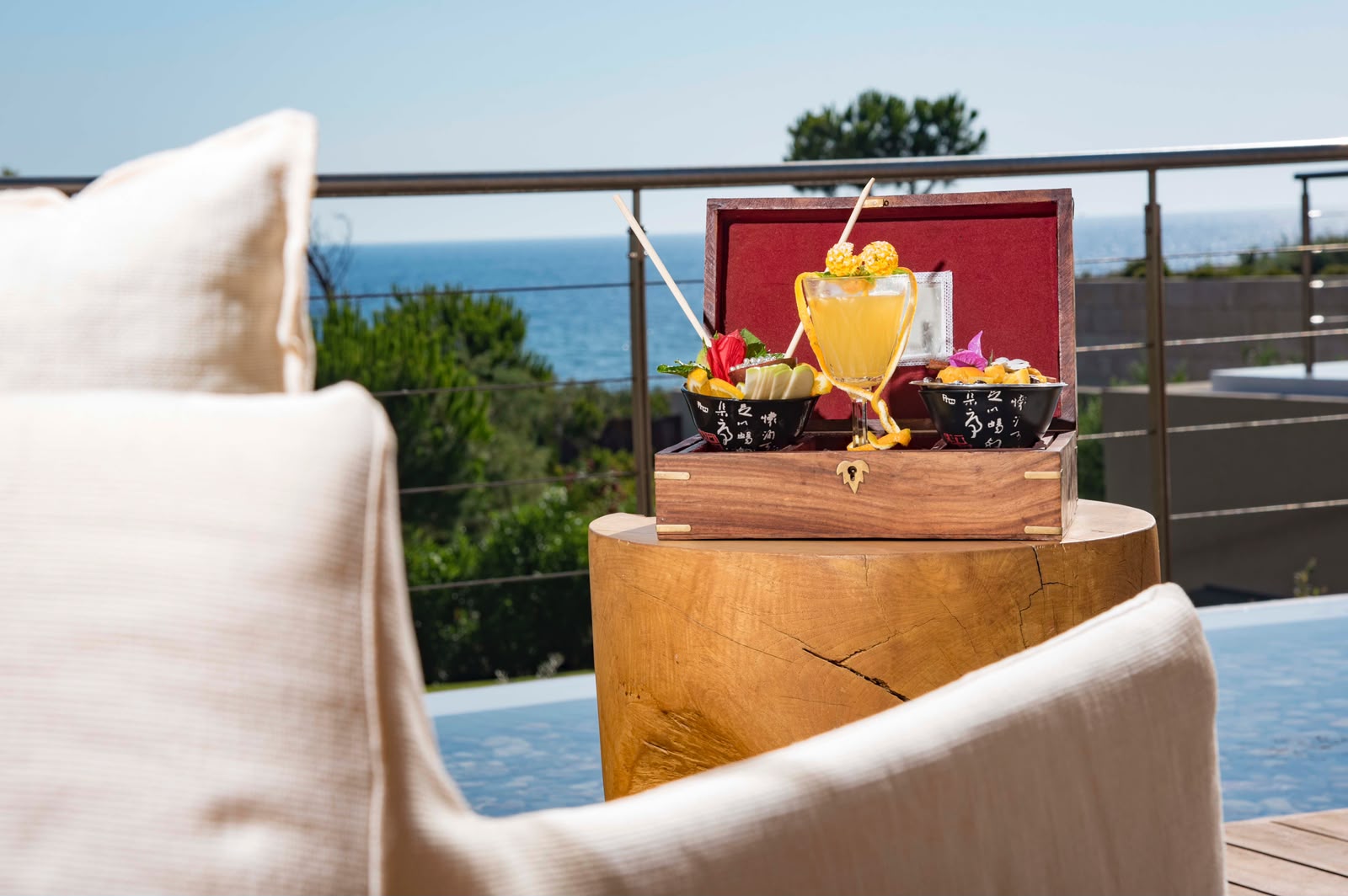 Signature cocktail served in a lacquered box with two garnish bowls above the sea