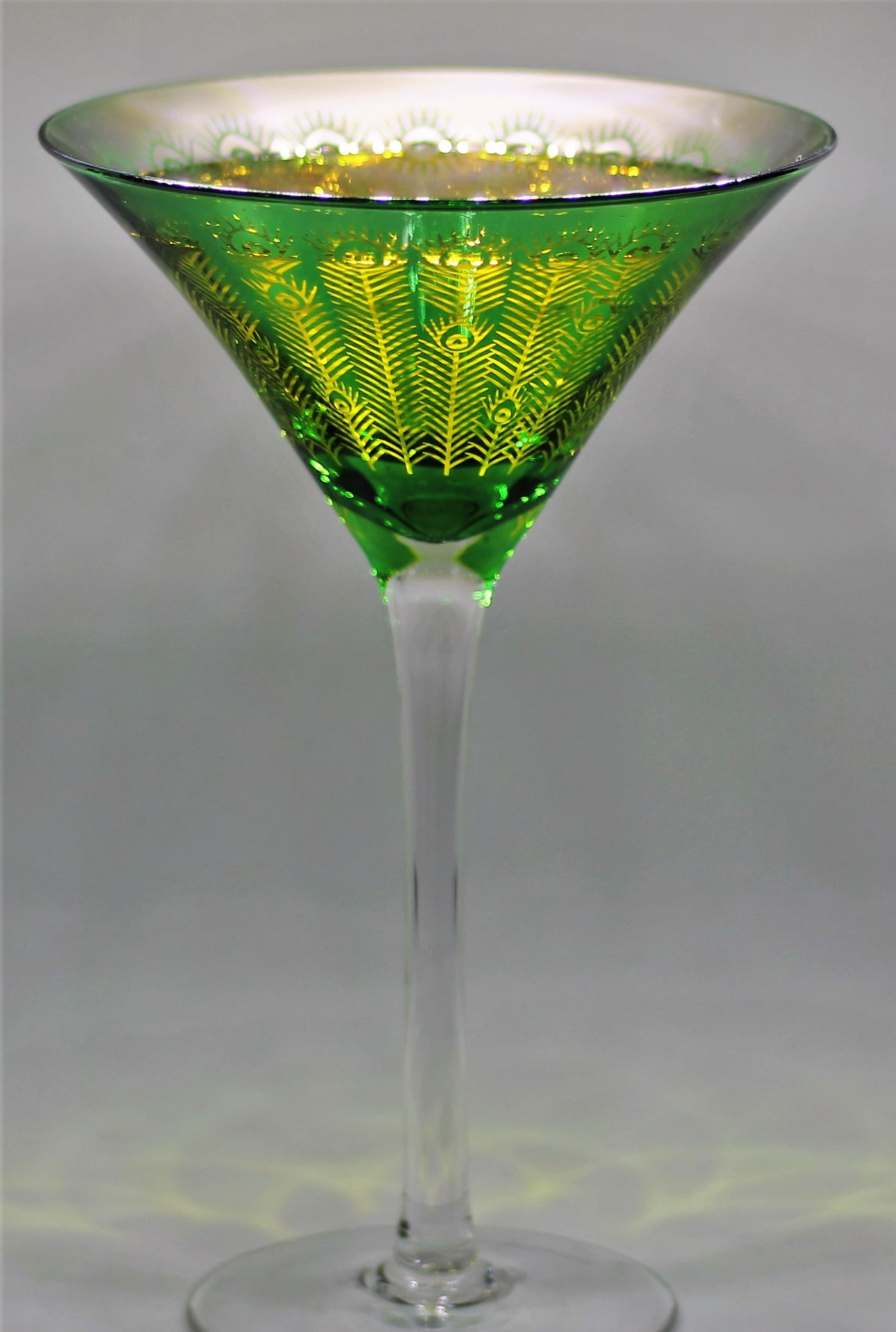 Tall peacock-etched glass holding a golden cocktail
