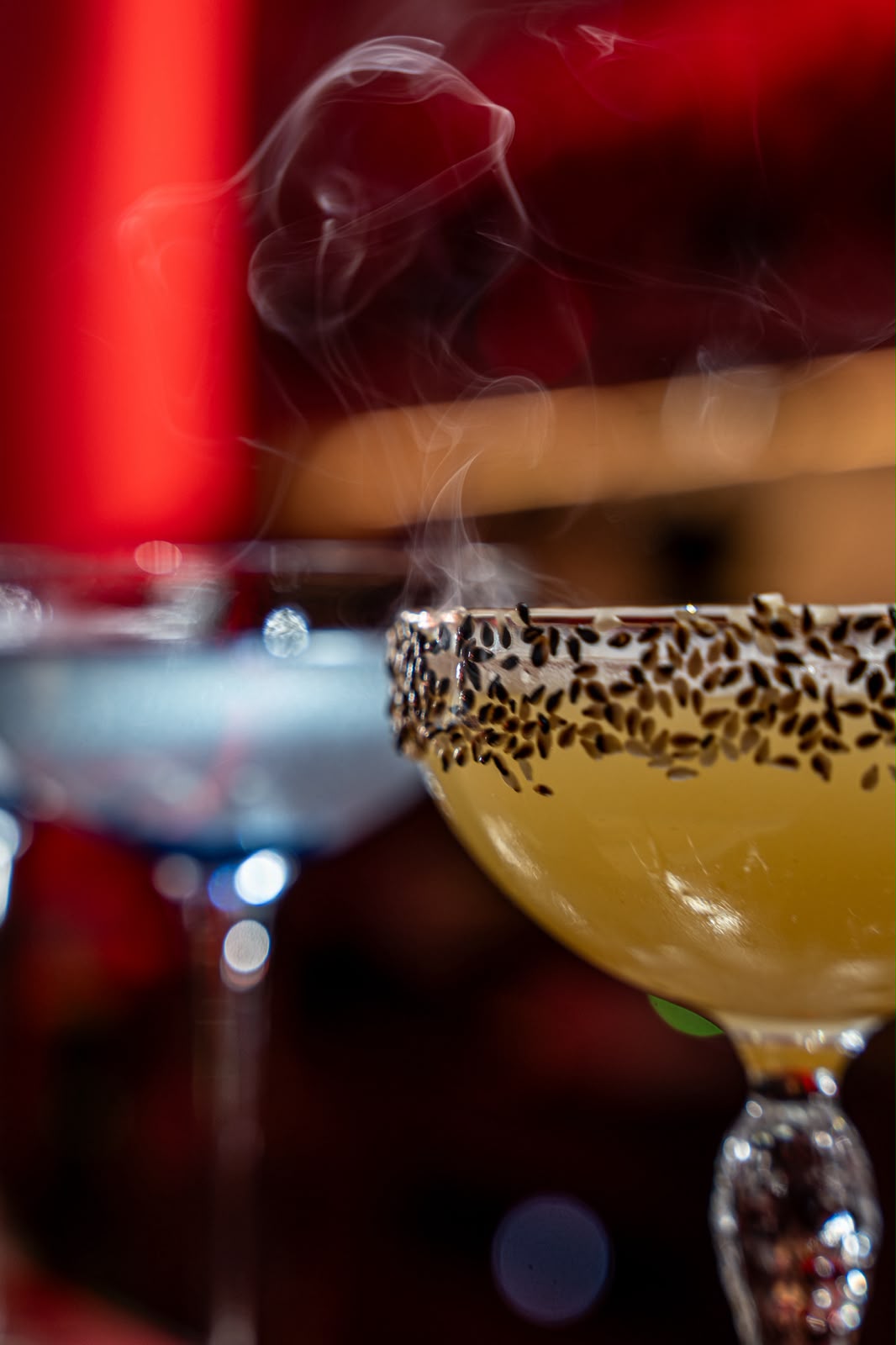 Smoked cocktail with a black sesame rim in red bar light