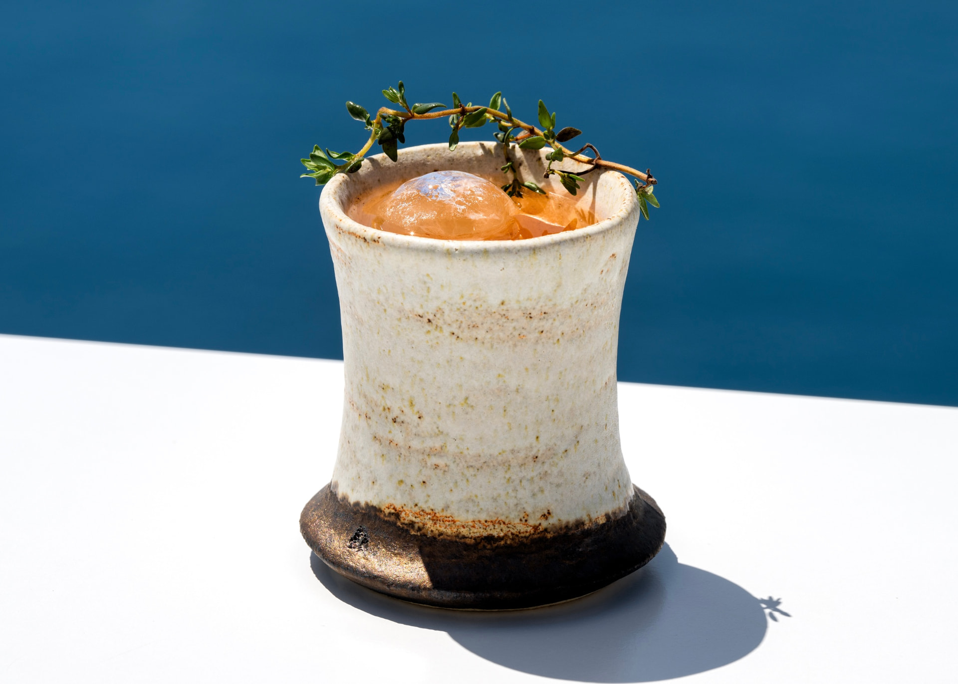 Amber cocktail in a handmade ceramic cup garnished with thyme
