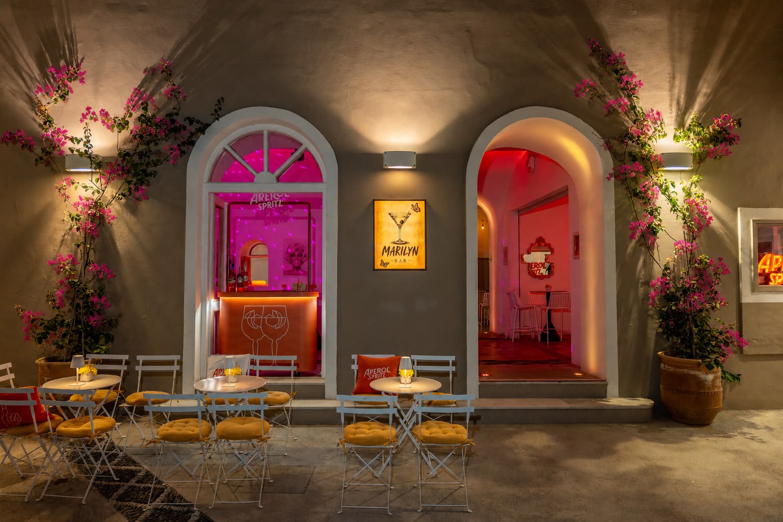 Marilyn Bar Santorini façade at night — lit arches, pink and red interiors, bougainvillea