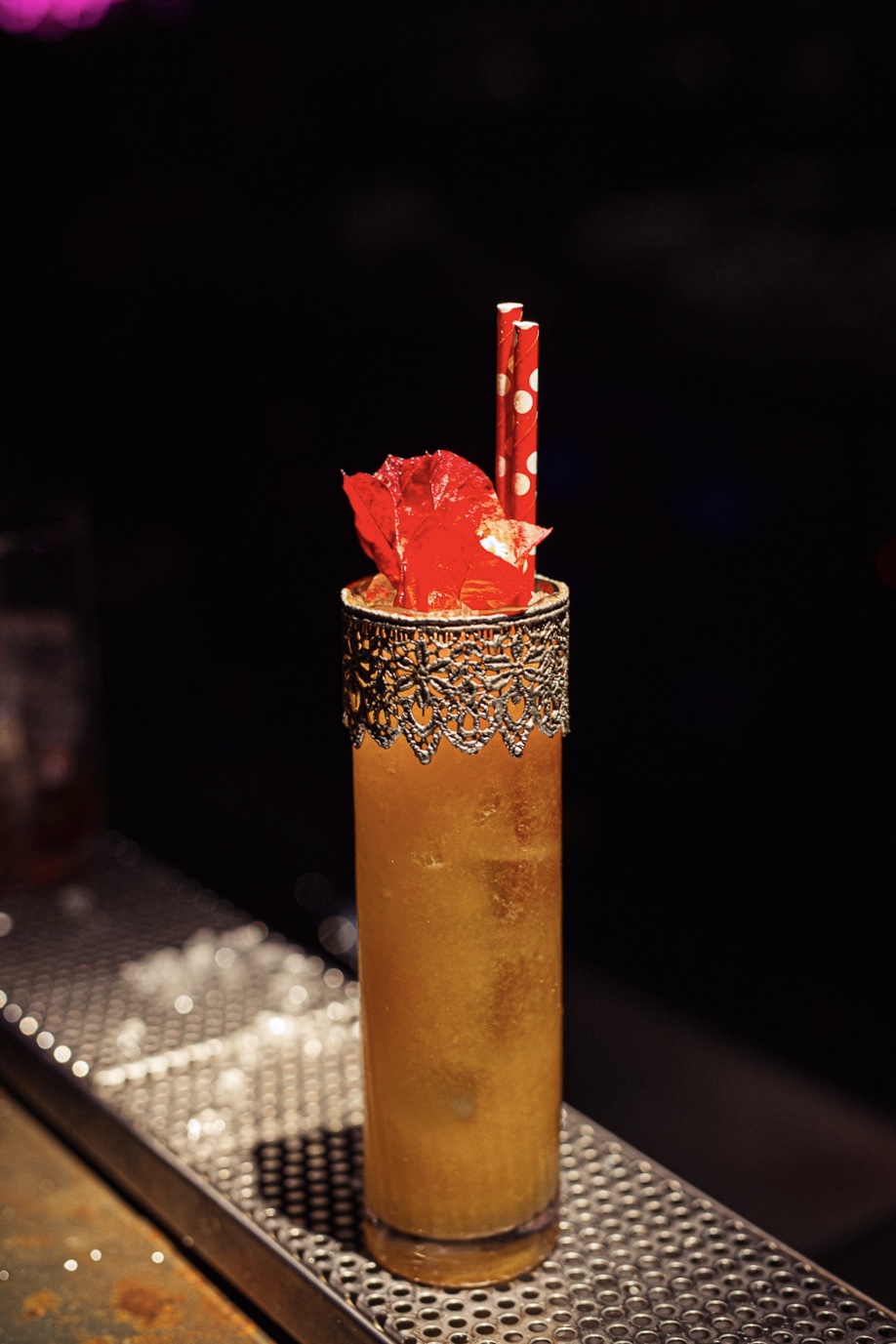 Tall amber cocktail in a lace-collared glass with a red leaf garnish