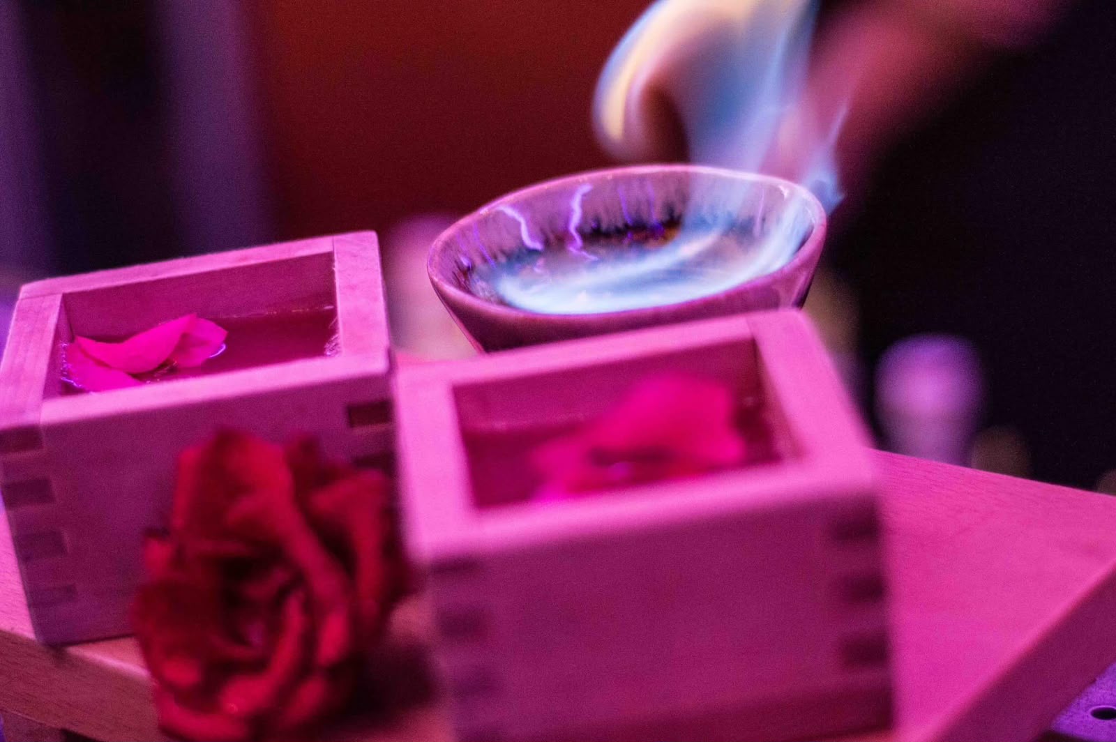 Flamed aromatic spoon poured over two wooden masu boxes with rose petals