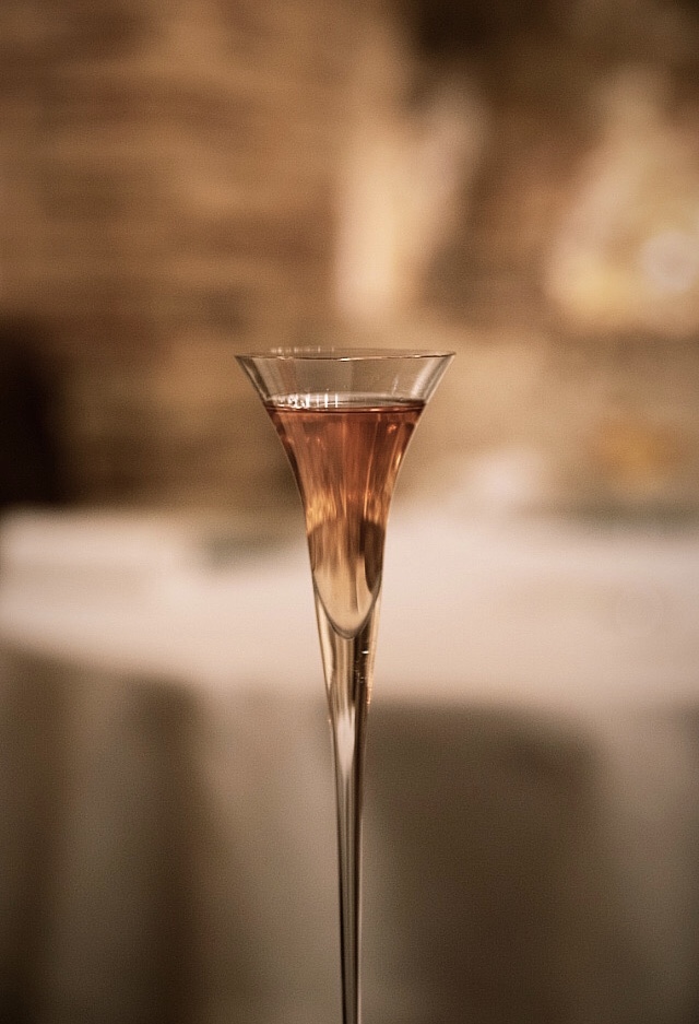 Detail of a rosé cocktail in a slim flute, warm dining room light