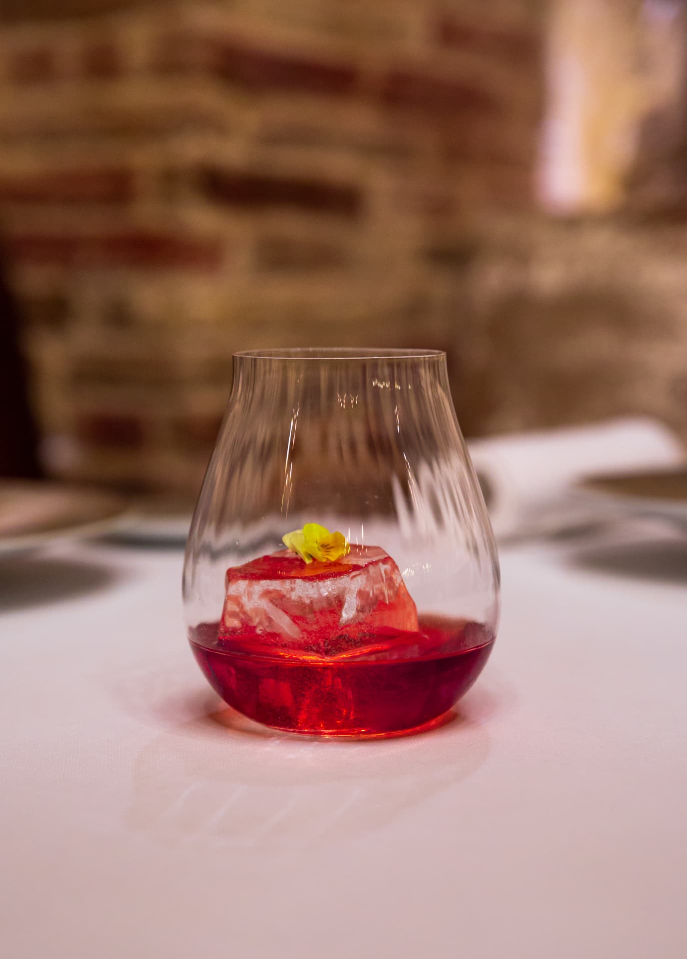 Red cocktail with a clear ice block and yellow flower on white linen