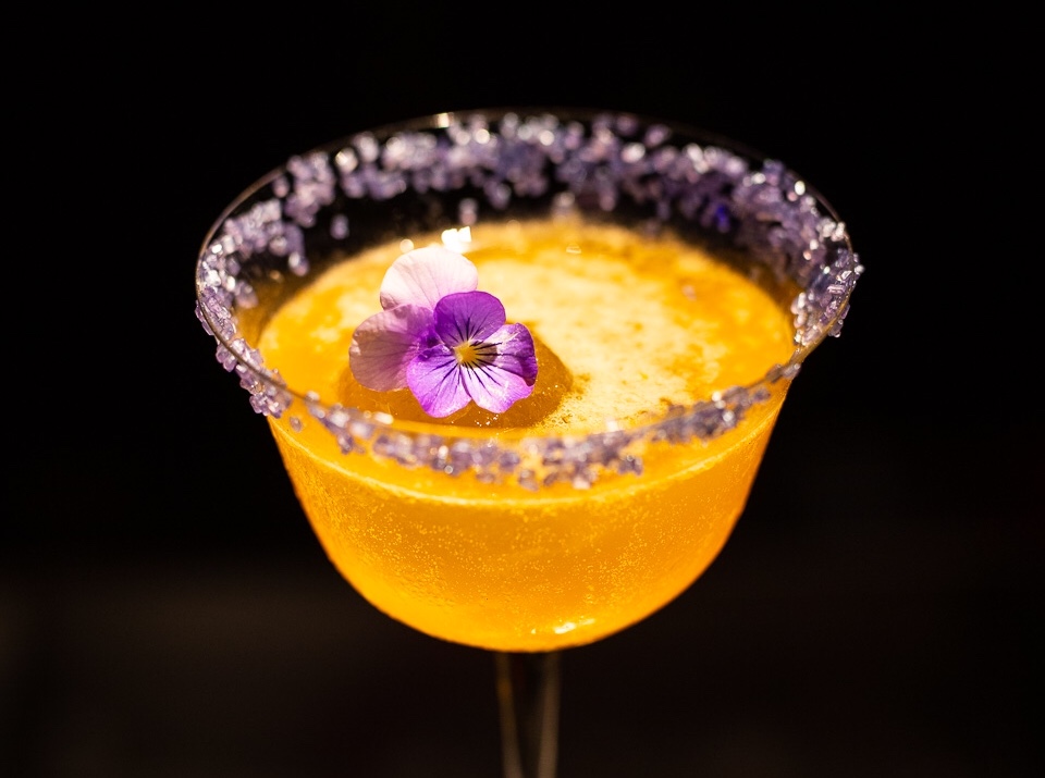 Close-up of a yellow cocktail with a lavender sugar rim and violet flower
