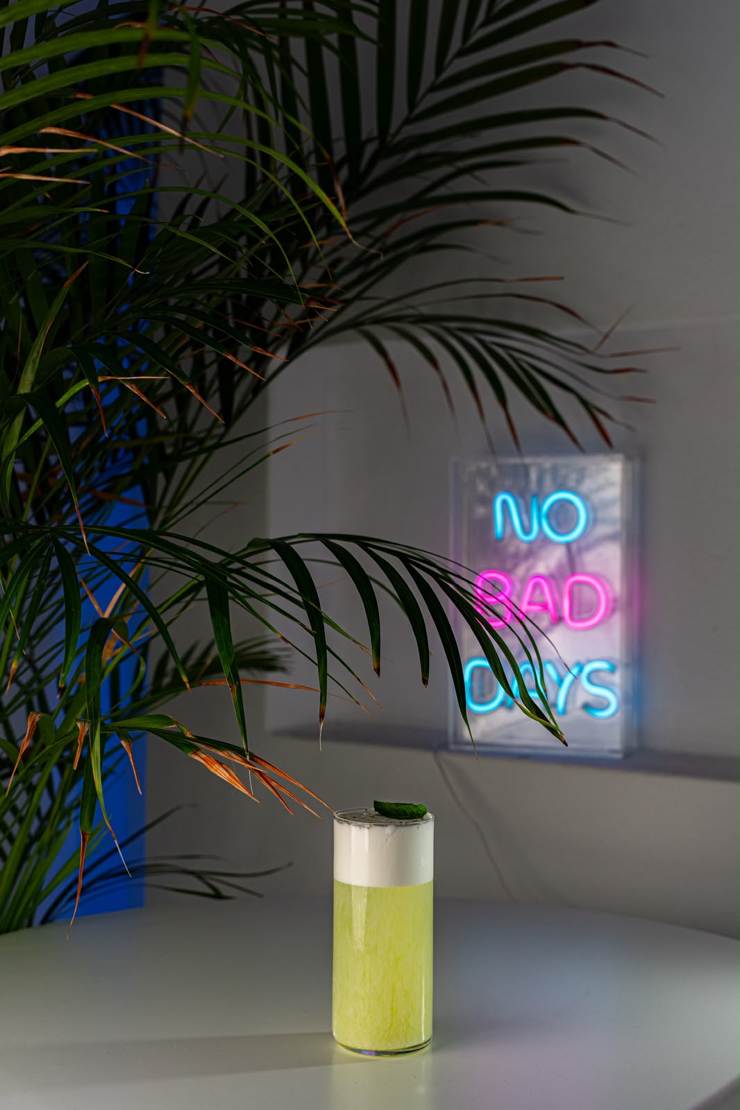 Green highball beside the 'No Sad Days' neon and palm leaves