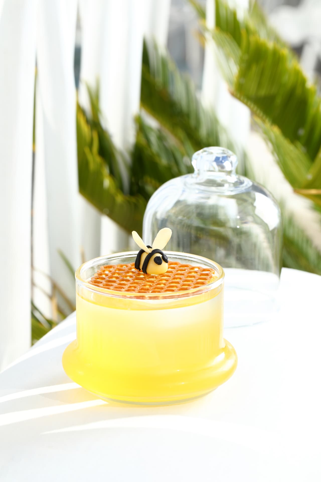 Honey-yellow cocktail sealed with honeycomb and a marzipan bee