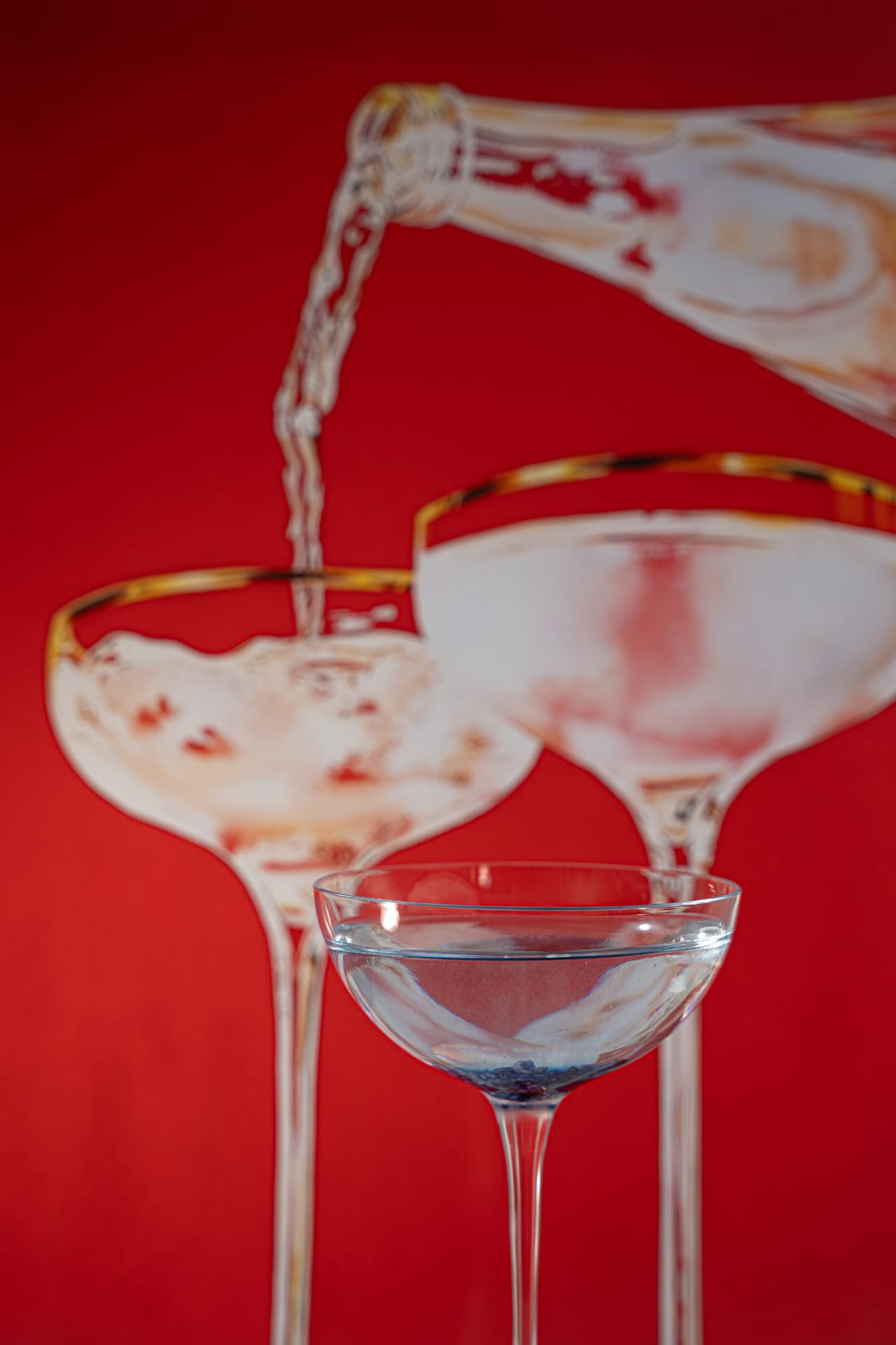 Sparkling wine poured into vintage coupes against a red backdrop