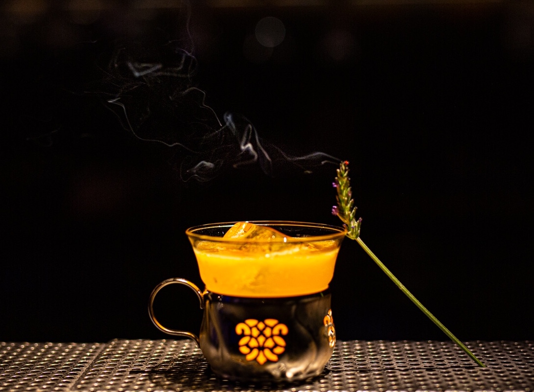 Smoking amber cocktail in an engraved cup with a lavender stem