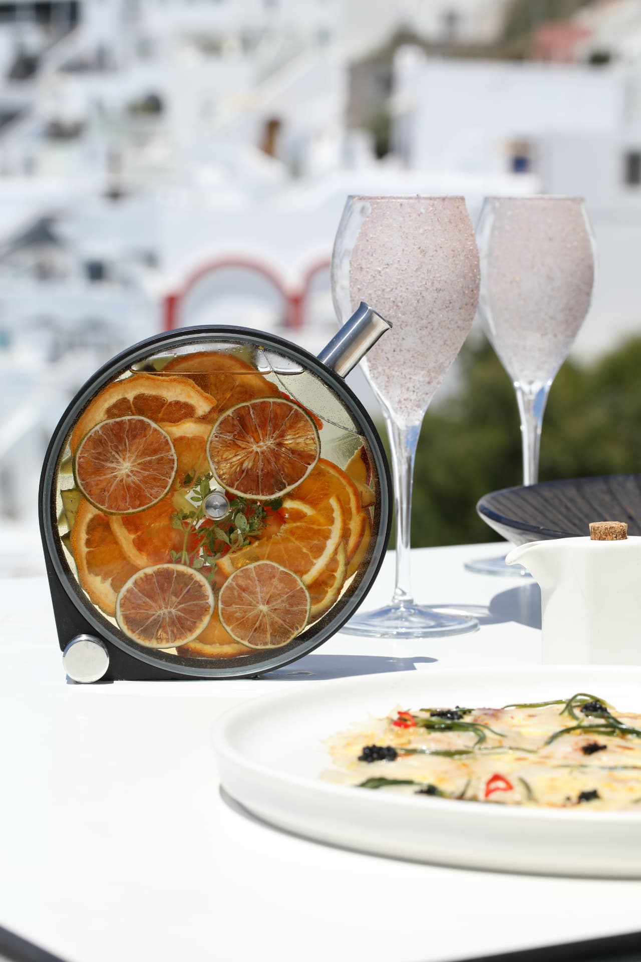 Citrus-filled punch vessel beside sparkling flutes and a raw fish plate