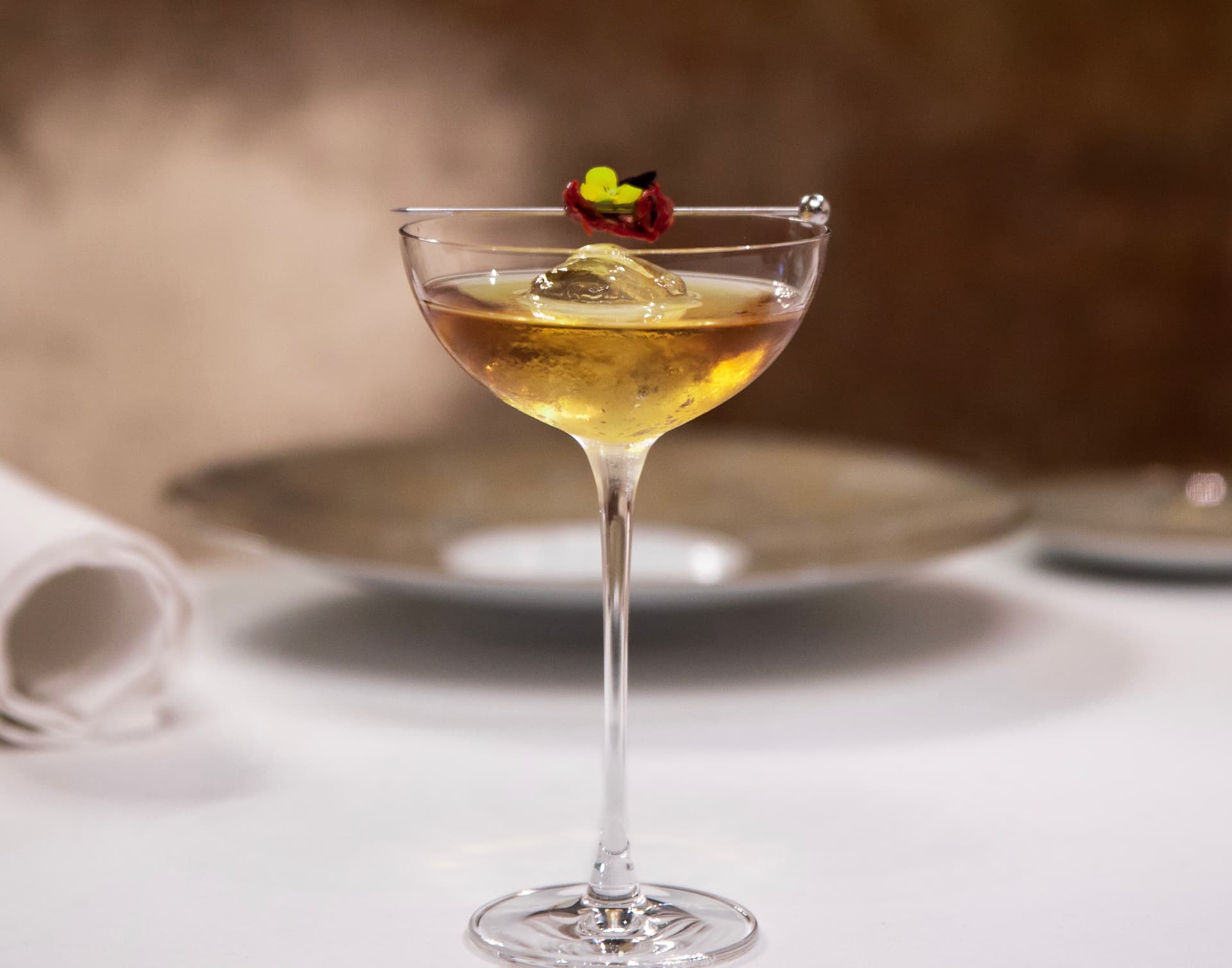 Amber cocktail in a coupe glass with a floral and dried tomato pick