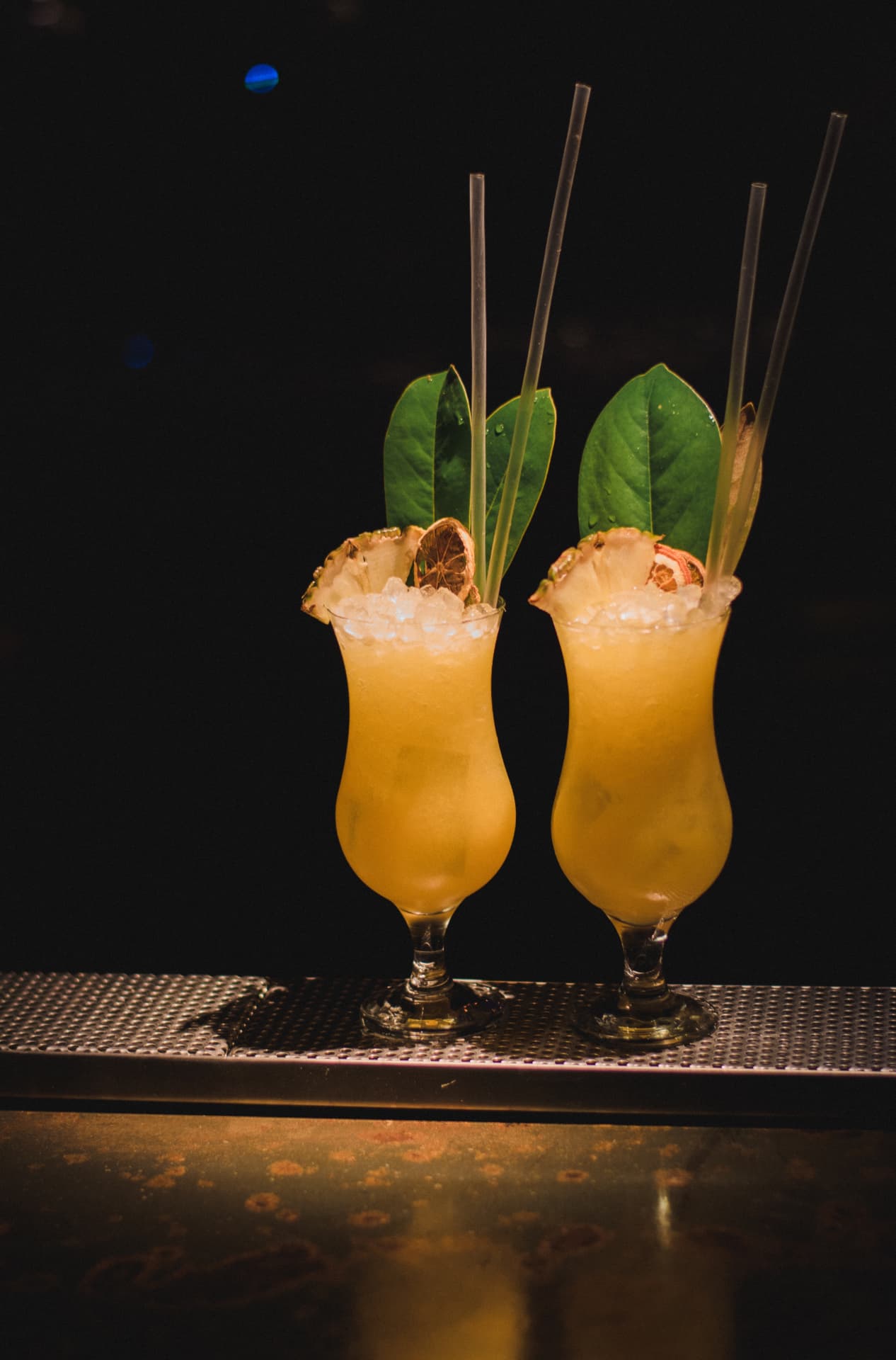 Pair of tall tropical cocktails with pineapple and leaf garnishes on the bar