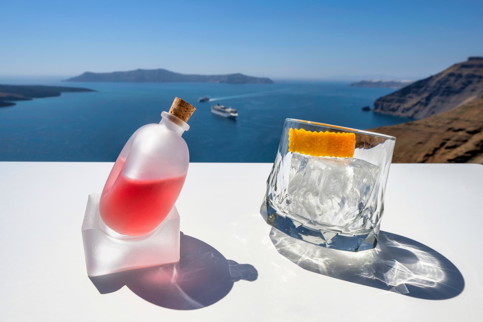 Frosted bottle serve and rocks glass with orange zest overlooking the sea