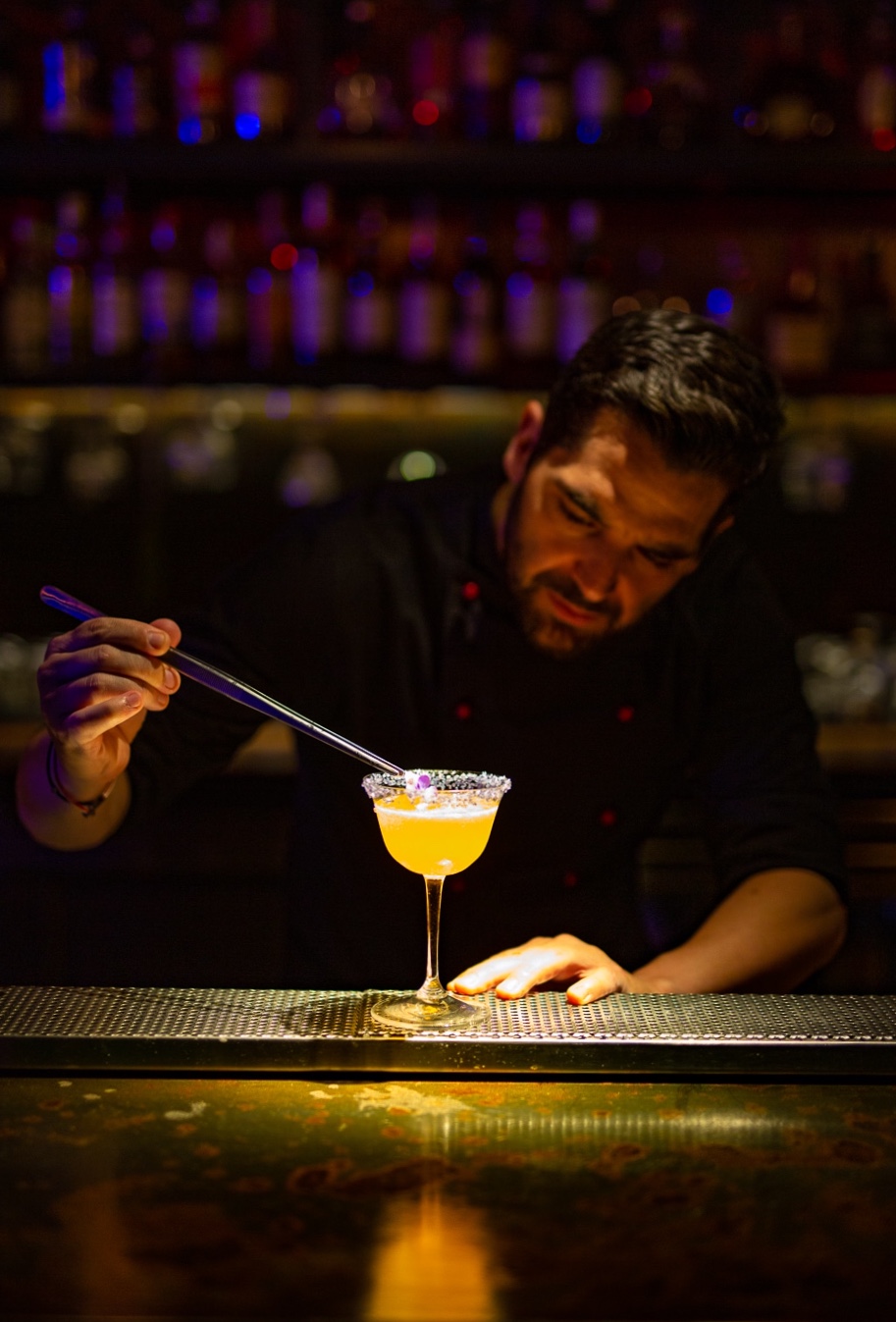 Bartender placing a flower garnish on a yellow cocktail behind the Fuga bar