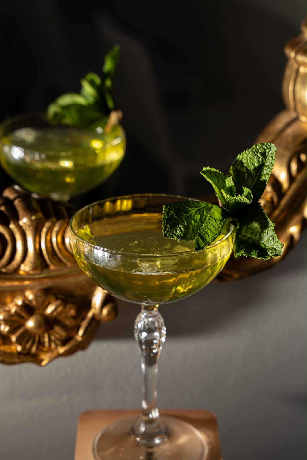 Herbal coupe cocktails with mint garnish on a gilded surface