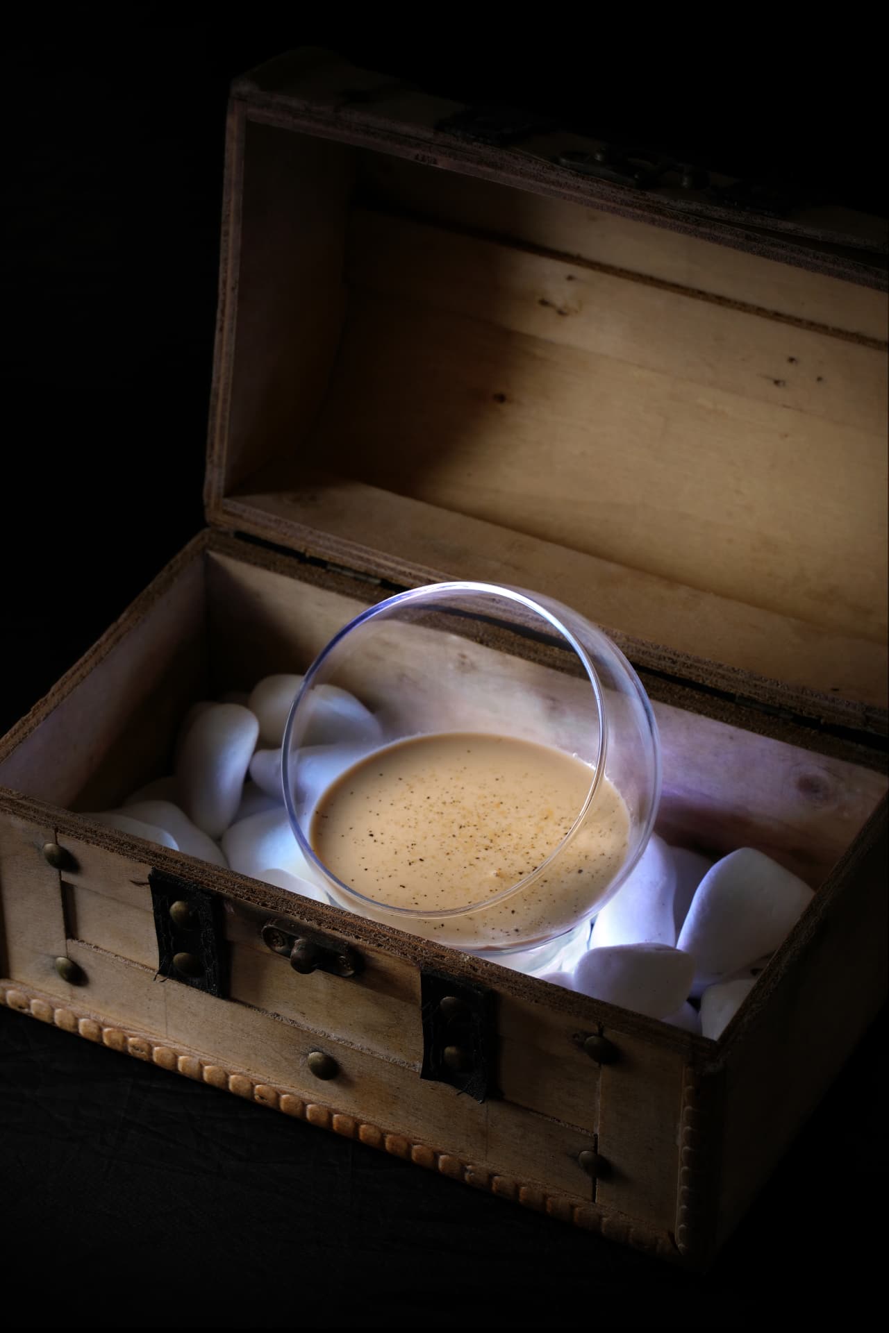 Creamy spiced cocktail lit inside a wooden chest of white stones
