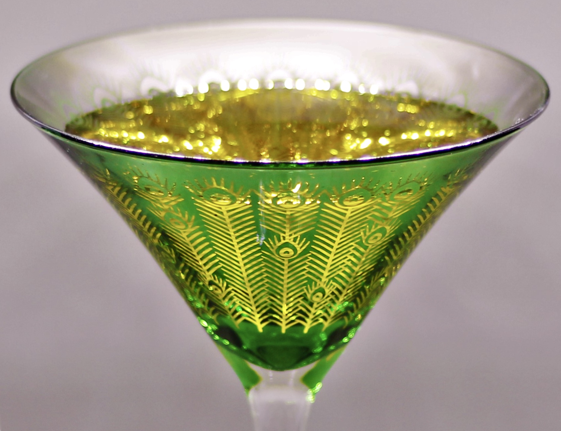 Peacock-etched green martini glass filled with a golden aperitif
