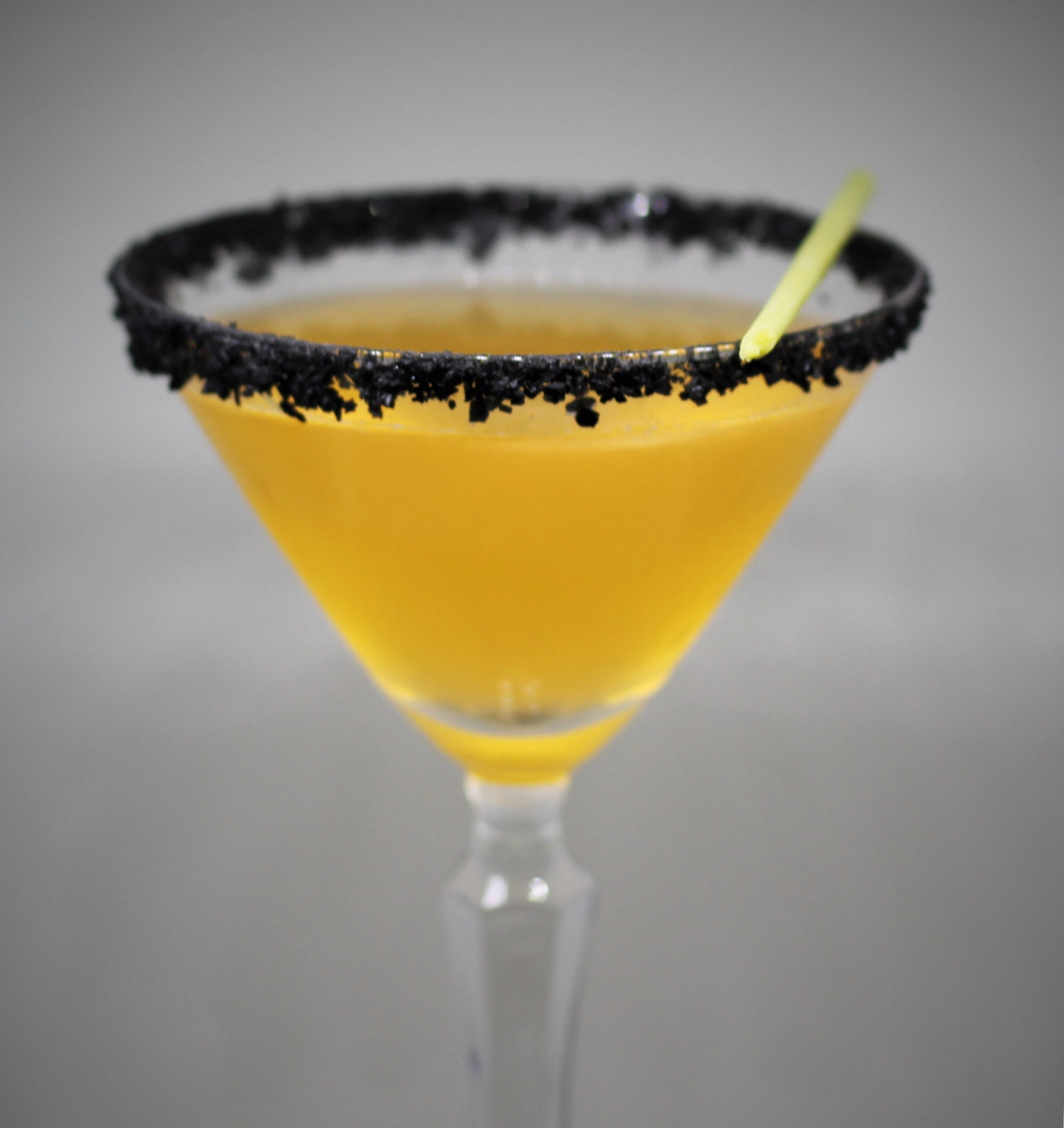 Yellow cocktail in a coupe with a black salt rim and lemongrass stem