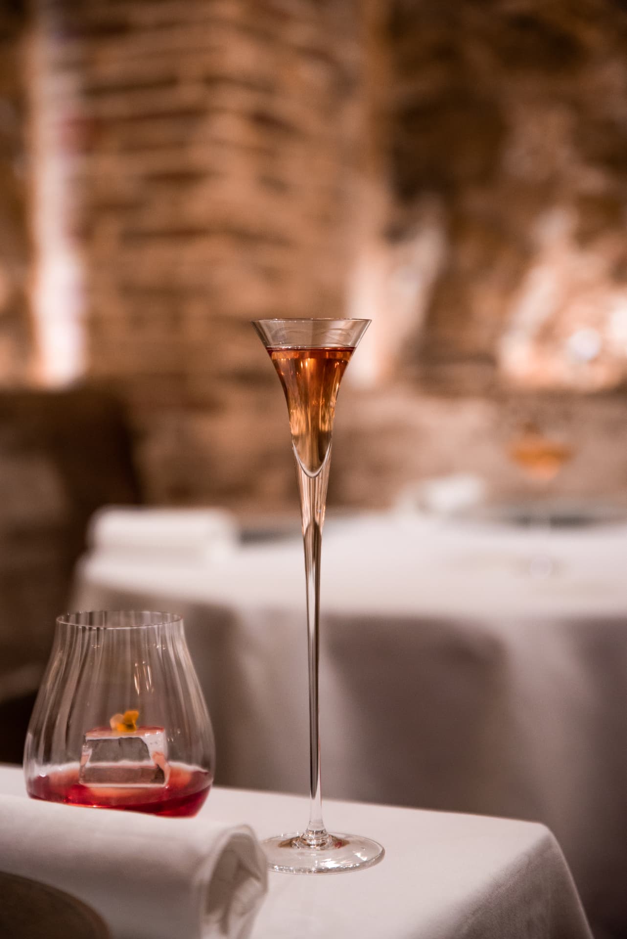 Tall stemmed rosé cocktail beside a red aperitif on a dressed table